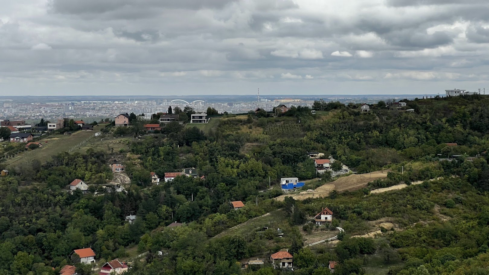 Häuser an den bewaldeten Hängen unter dem Aussichtspunkt, dahinter Novi Sad und die Bögen der Žeželj-Brücke