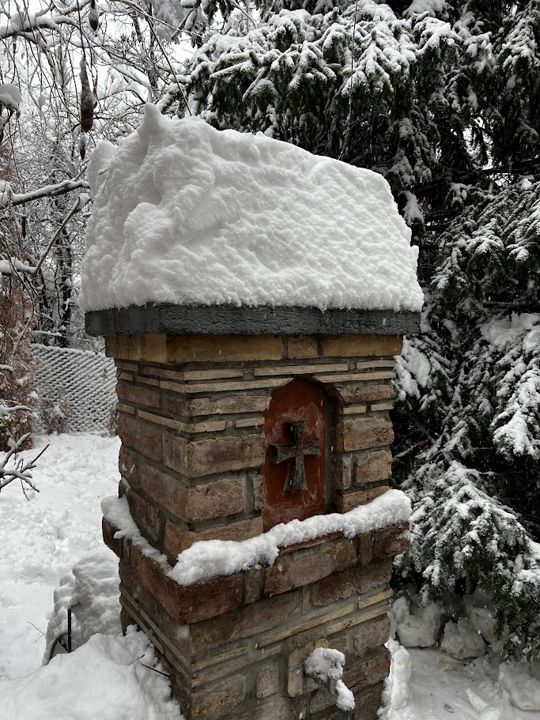 Eine Schneehaube auf einem Ziegelpfeiler mit Kreuz
